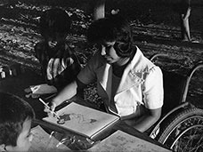 una niña dibujando mientras está sentada en una silla de ruedas.