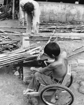Man standing and boy in wheelchair working with cane.