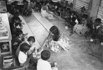 Children in a large circle attended by two women.