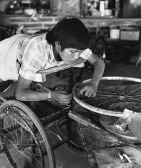 Boy lying face down on board works with bicycle wheels with hands.