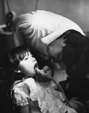 Dental worker with one arm looking into girl's mouth.