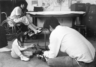 Man working with young girl, woman in wheelchair at back.